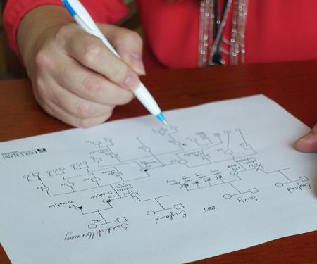 A person holds a pen to a piece of paper as they map various hereditary genes on it.
