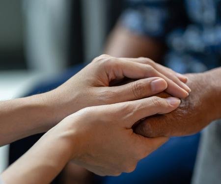 A closeup photo of a person using both of their hands to gently clasp around another person's hand.