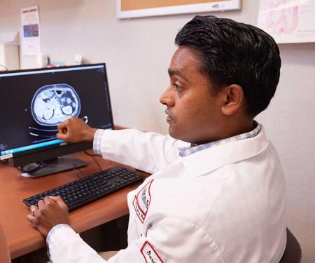 A photo of a Fox Chase doctor and a patient sitting at a desk, while the doctor gestures at the screen.