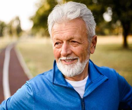 A portrait shot of a man with his hands on his hips standing on a running track, smiling as he looks off camera.