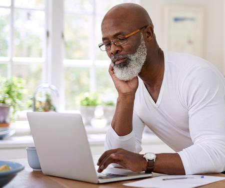 A person leans down to use their laptop on a kitchen counter.