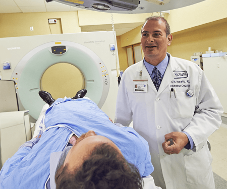 A photo of a Fox Chase doctor smiling as he stands next to a patient about to go into a medical imaging machine.