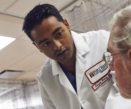 A photo of Dr. Sanjay Reddy leaning over a patient laying down on a hospital bed.
