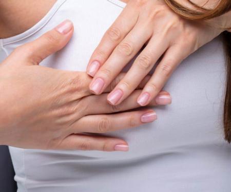 A close of up a person wearing a white tank top, with both of their hands over one their breasts.