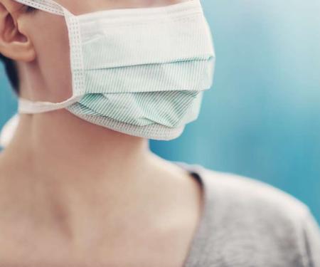 A portrait shot of a person's face cut off above the nose, covered by a mask and looking off to the side.