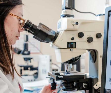 A photo of a Fox Chase doctor looking through a microscope, with a screen displaying chromosomes to their right.