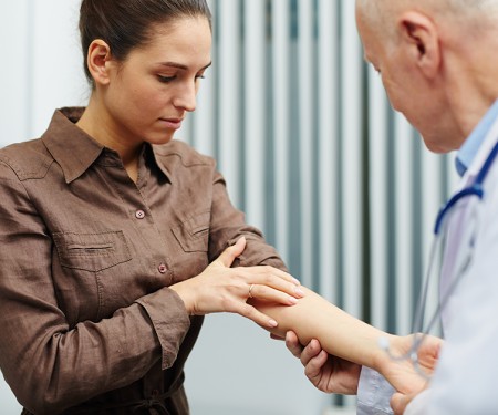 A medical professional exams the inside of a patient's forearm in a medical room.