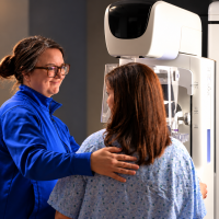 A woman guiding another woman through a mammogram