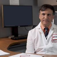 A photograph of a Fox Chase doctor sitting behind a desk, speaking with someone on the other side of it.