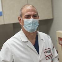 A photo looking over the shoulder of a patient as a masked Fox Chase doctor looks at them, both standing in a medical room.