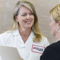 A photograph of a Fox Chase doctor holding a file, smiling at a patient.