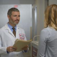 A Fox Chase doctor stands facing another person in a hallway, holding a file in his hands.