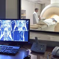 A photograph of a medical professional standing next to a patient inside of a large medical imaging machine.