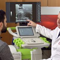 A photograph of a Fox Chase doctor speaking to a patient in a medical chair while gesturing at an image on a screen.