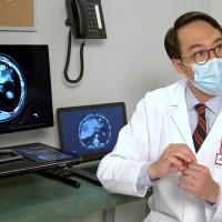 A photograph of a Fox Chase doctor looking off camera, with two screens on a desk to his left showing medical imaging results.