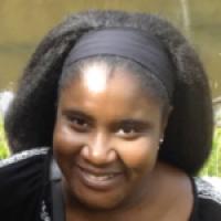 A close up photograph of Sajitha Anthony's face, smiling at the camera as they stand outside.