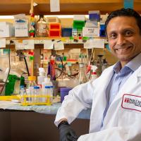Close-up of Siddharth Balachandran sitting at a desk, wearing a white coat and smiling