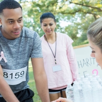 A photograph of three runners at a table with water bottles on it, with a person behind the table speaking to one of them.