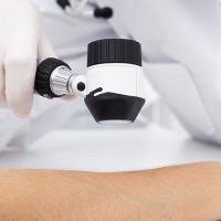 A closeup photo of a medical professional holding a handheld tool up to a patient's arm to help them examine it.