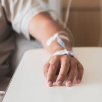 A closeup photo of a patient's arm as they sit in a chair and receive an IV through their wrist.