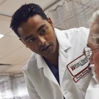 A photo of Dr. Sanjay Reddy leaning over a patient laying down on a hospital bed.