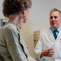 A side view photograph of a patient sitting in a tan medical chair, speaking with a Fox Chase doctor on the other side of them.