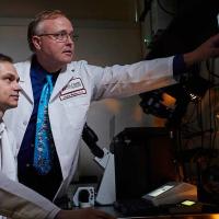 A photograph of two Fox Chase doctors sitting in a dim room, one gesturing at a screen with various blue splotches displayed.