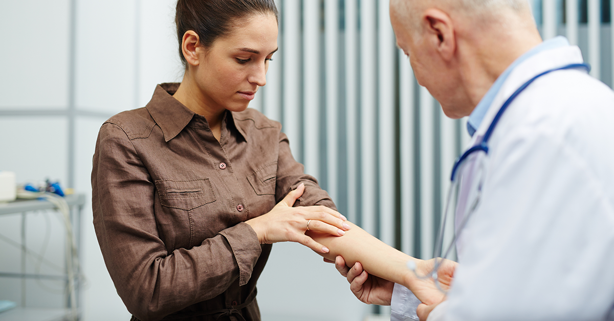 A medical professional exams the inside of a patient's forearm in a medical room.